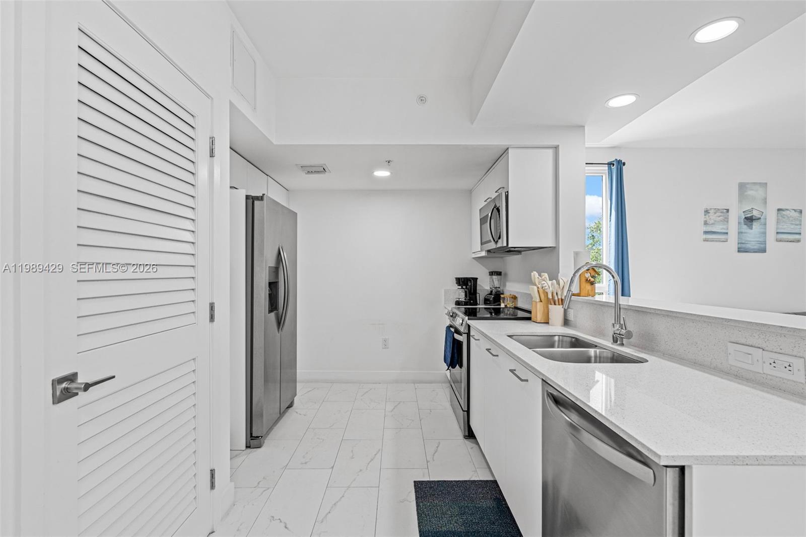A modern kitchen features white cabinets, stainless steel appliances, and light-colored tiled flooring — 1850 Monroe Street # 309, Hollywood FL 33020, HOLLYWOOD, FL