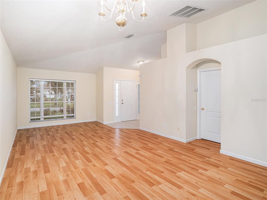 An empty living room features light-colored walls, wood-look flooring, a vaulted ceiling, and a chandelier — 11440 MISTY ISLE LANE, RIVERVIEW, FL