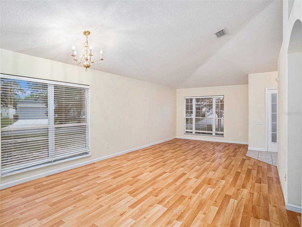 An empty room with light wood-look flooring, cream walls, a chandelier, and two windows — 11440 MISTY ISLE LANE, RIVERVIEW, FL