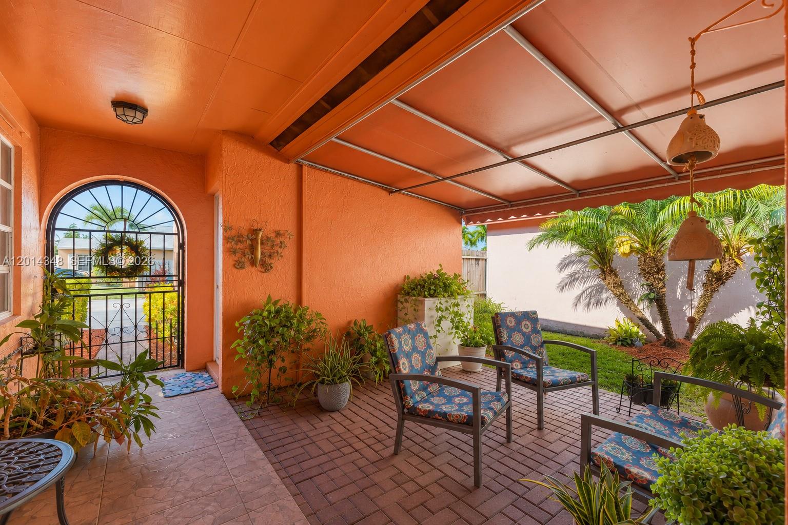 A covered patio features orange walls, brick flooring, outdoor furniture, and a metal gate — 12801 SW 248th Ter, Homestead FL 33032, HOMESTEAD, FL