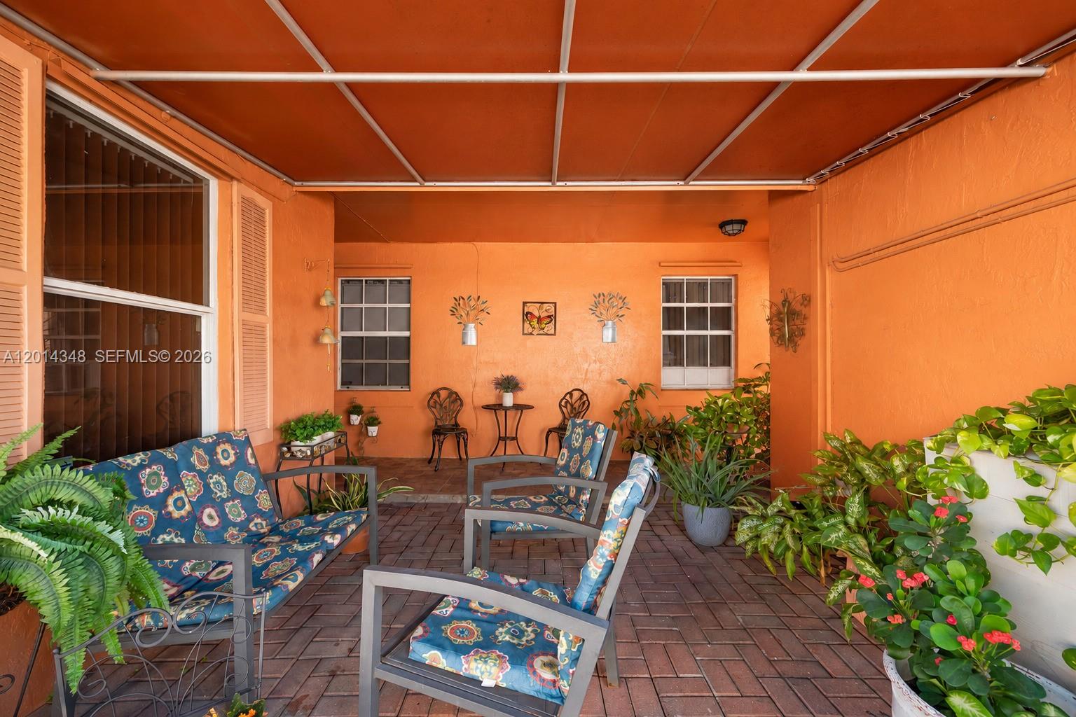 A covered outdoor patio features orange walls, brick flooring, and various seating arrangements — 12801 SW 248th Ter, Homestead FL 33032, HOMESTEAD, FL