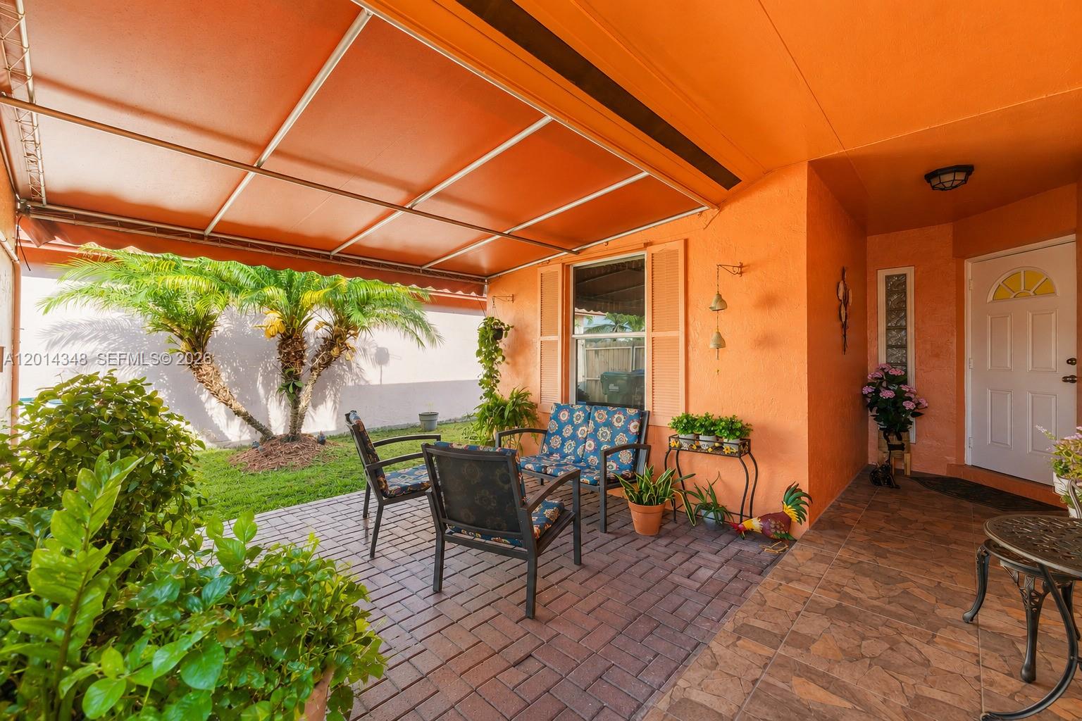 A covered patio features brick pavers, outdoor seating, and an orange exterior wall — 12801 SW 248th Ter, Homestead FL 33032, HOMESTEAD, FL