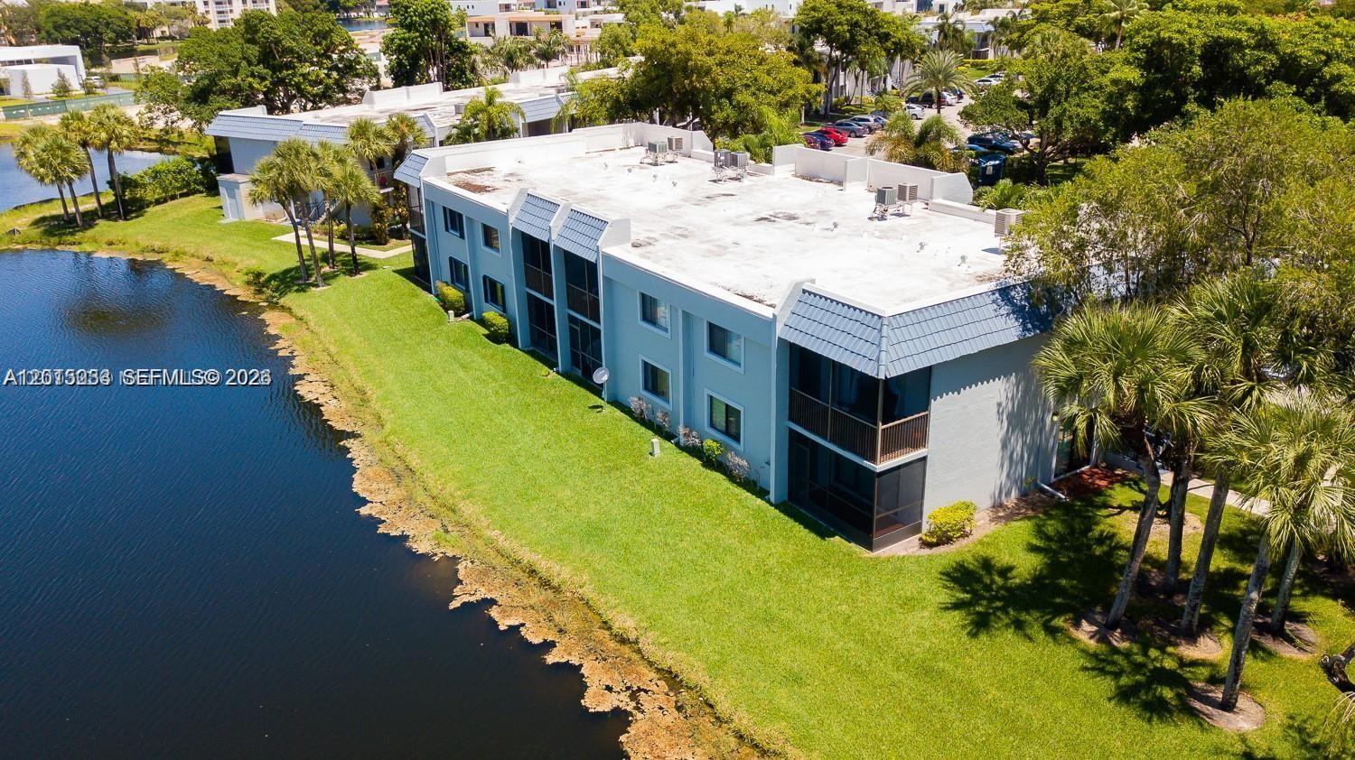 An aerial view shows a multi-story apartment building situated next to a lake — 16561 Blatt Blvd # 201, Weston FL 33326, WESTON, FL