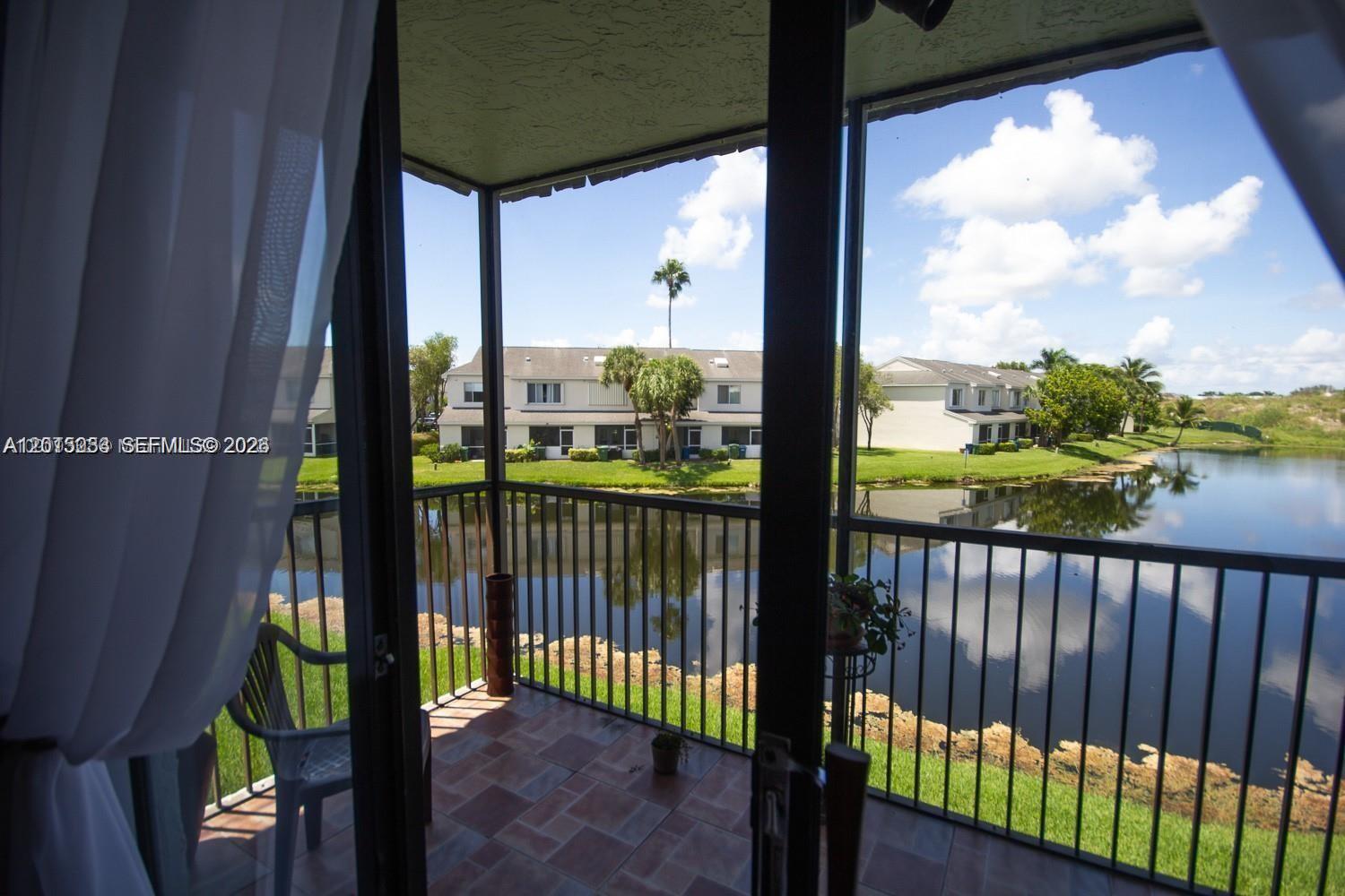A screened-in balcony overlooks a pond and residential buildings under a blue sky — 16561 Blatt Blvd # 201, Weston FL 33326, WESTON, FL