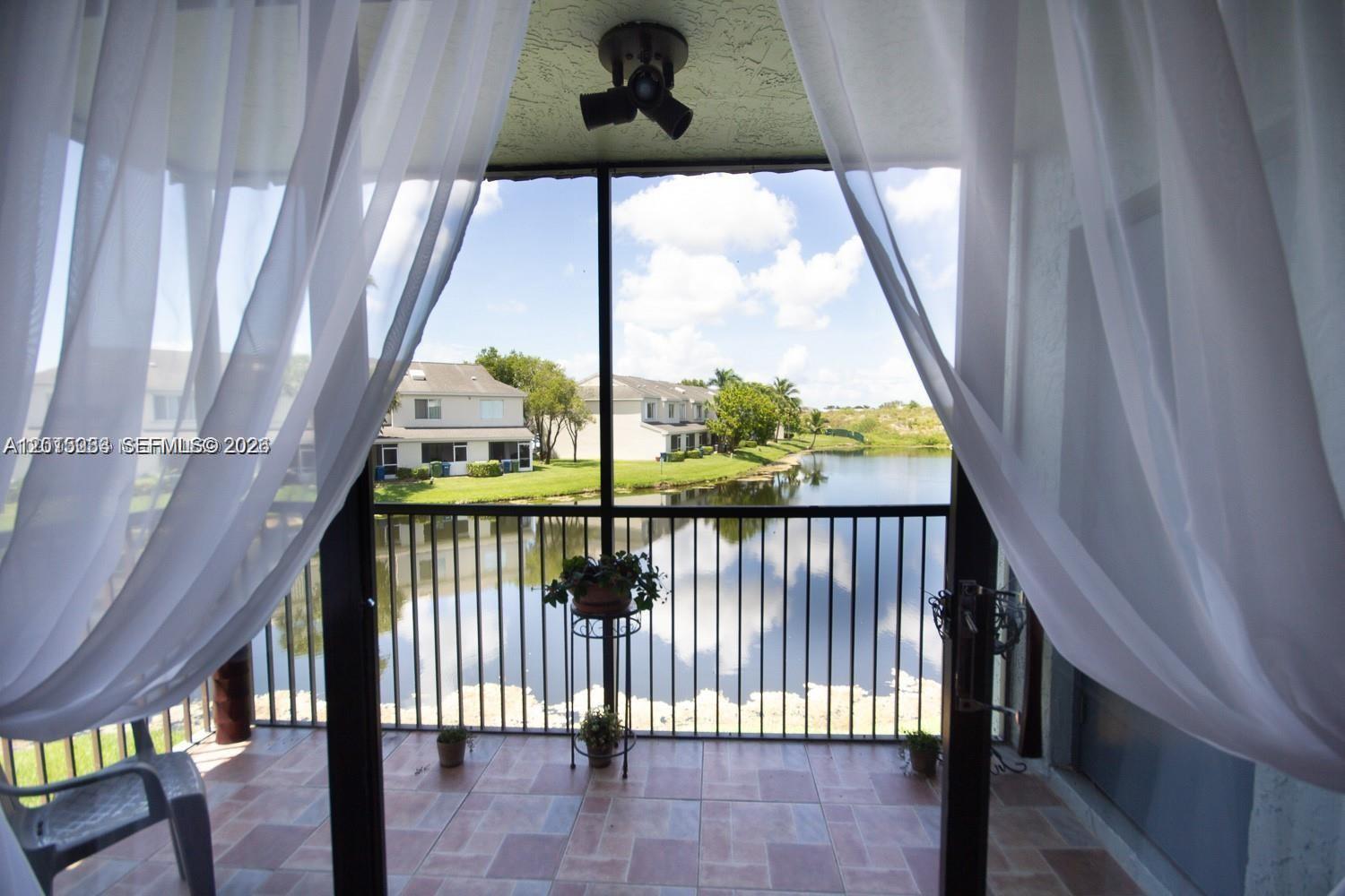 A screened-in balcony with tile flooring overlooks a lake and neighboring residential buildings — 16561 Blatt Blvd # 201, Weston FL 33326, WESTON, FL