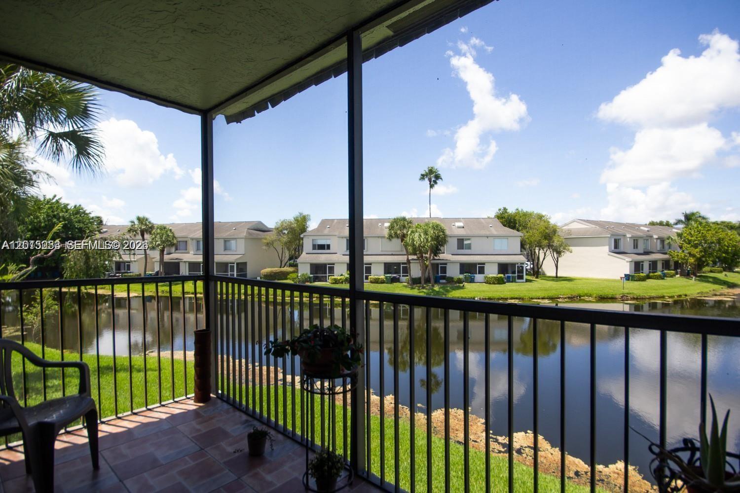A covered balcony with tile flooring overlooks a lake and neighboring residential buildings — 16561 Blatt Blvd # 201, Weston FL 33326, WESTON, FL
