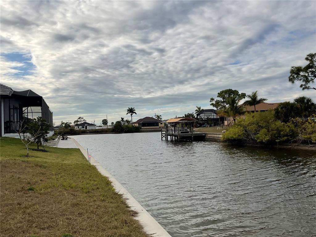 A view of a canal with a wooden dock and residential homes in the background — 3431 NW 17TH LANE, CAPE CORAL, FL