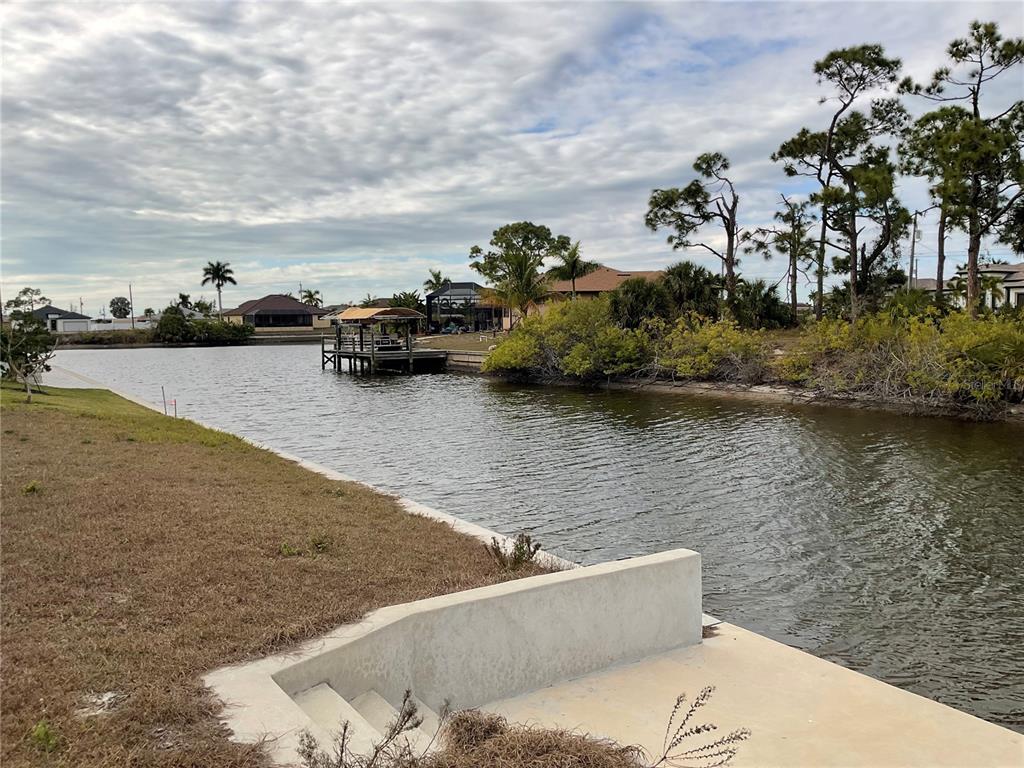A concrete bulkhead and steps overlook a canal with a boat dock and houses — 3431 NW 17TH LANE, CAPE CORAL, FL