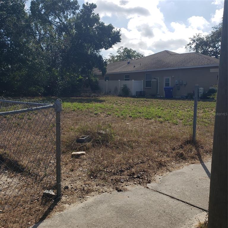A vacant, grassy residential lot sits next to a house with a white fence — VIRGINIA AVENUE, TARPON SPRINGS, FL