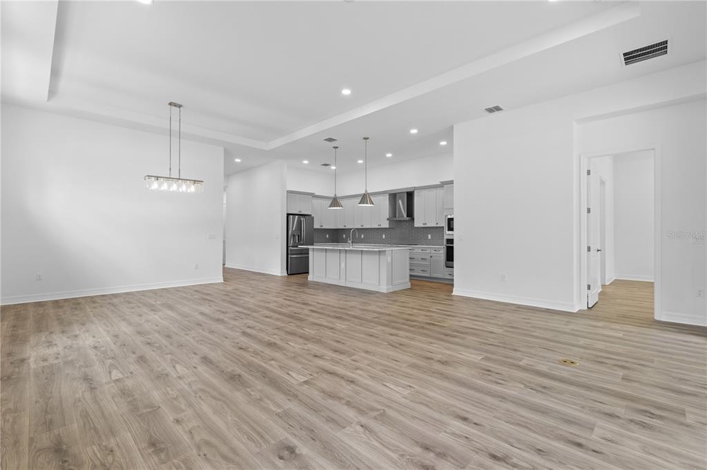 An open-concept kitchen and living area features light wood flooring, white cabinetry, and pendant lighting — 1068 LILIANA DRIVE, DELAND, FL