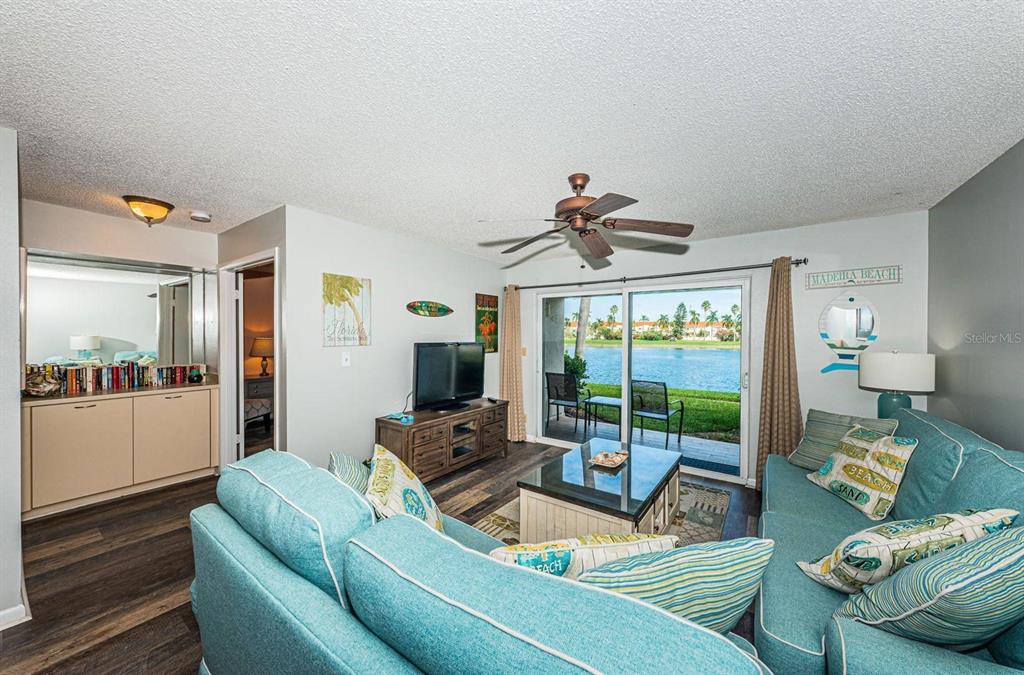 A living room with a teal sofa, wood-look flooring, and a sliding door overlooking water — 6100 BAHIA DEL MAR CIRCLE UNIT 103, ST PETERSBURG, FL