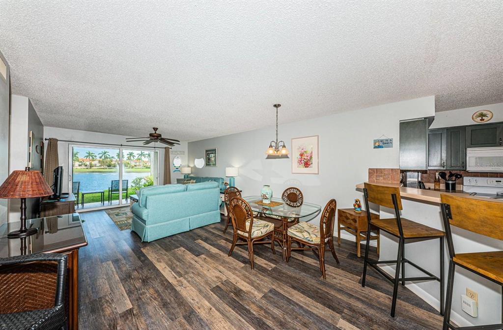 An open-concept living and dining area with wood-look flooring and a view of a lake — 6100 BAHIA DEL MAR CIRCLE UNIT 103, ST PETERSBURG, FL