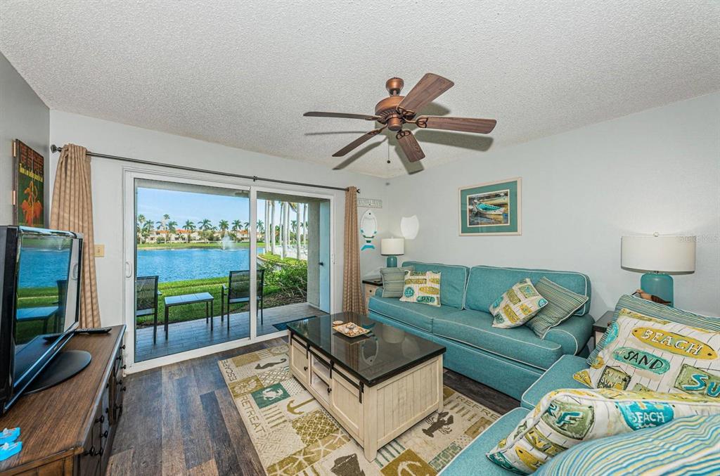 A living room with a teal sofa, coffee table, and sliding doors overlooking a lake — 6100 BAHIA DEL MAR CIRCLE UNIT 103, ST PETERSBURG, FL