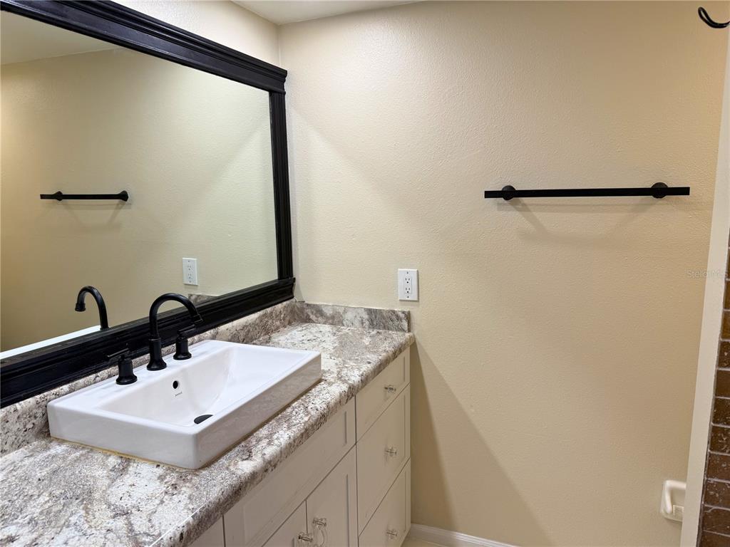 A bathroom vanity features a white vessel sink, black fixtures, and a large framed mirror — 4821 W MCELROY AVENUE UNIT D210, TAMPA, FL
