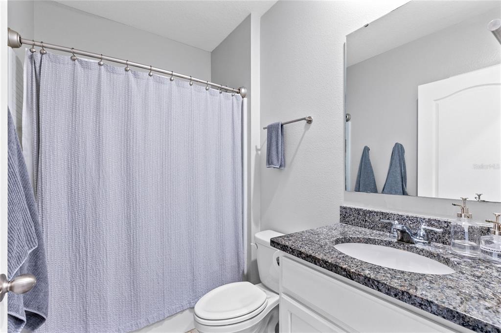 A bathroom features a granite vanity, a white toilet, and a shower with a blue curtain — 5207 MAHOGANY DRIVE, MOUNT DORA, FL