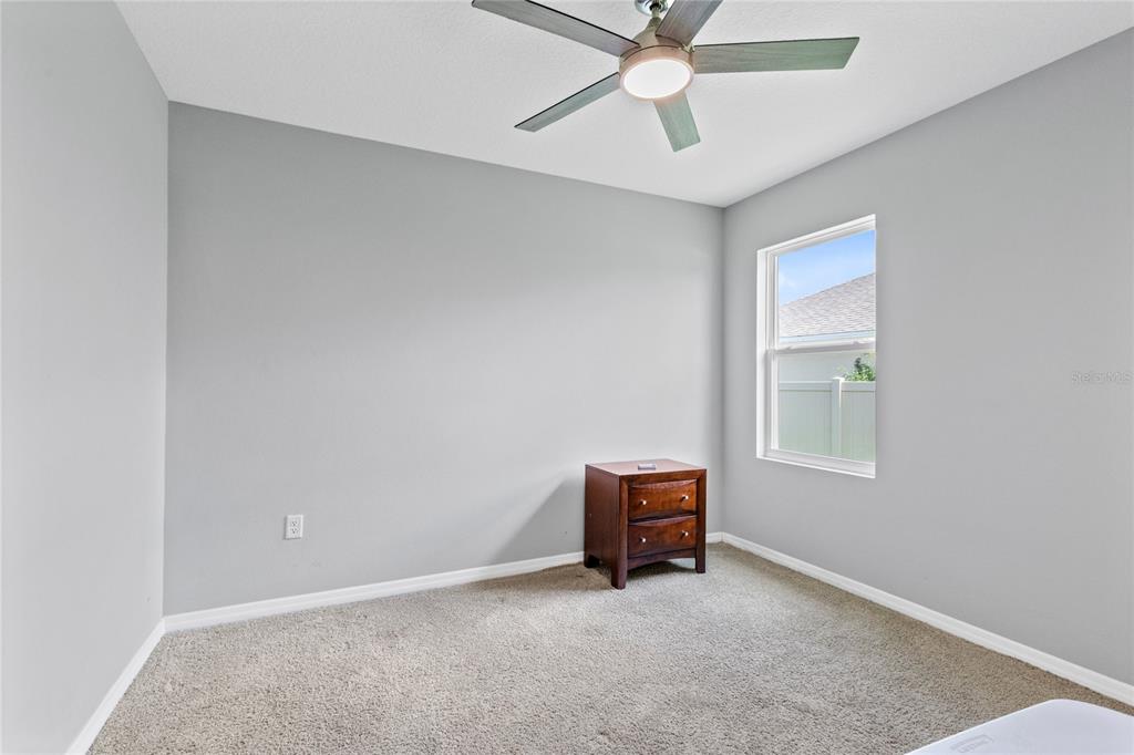 A bedroom with gray walls, beige carpeting, a ceiling fan, and a wooden nightstand — 5207 MAHOGANY DRIVE, MOUNT DORA, FL