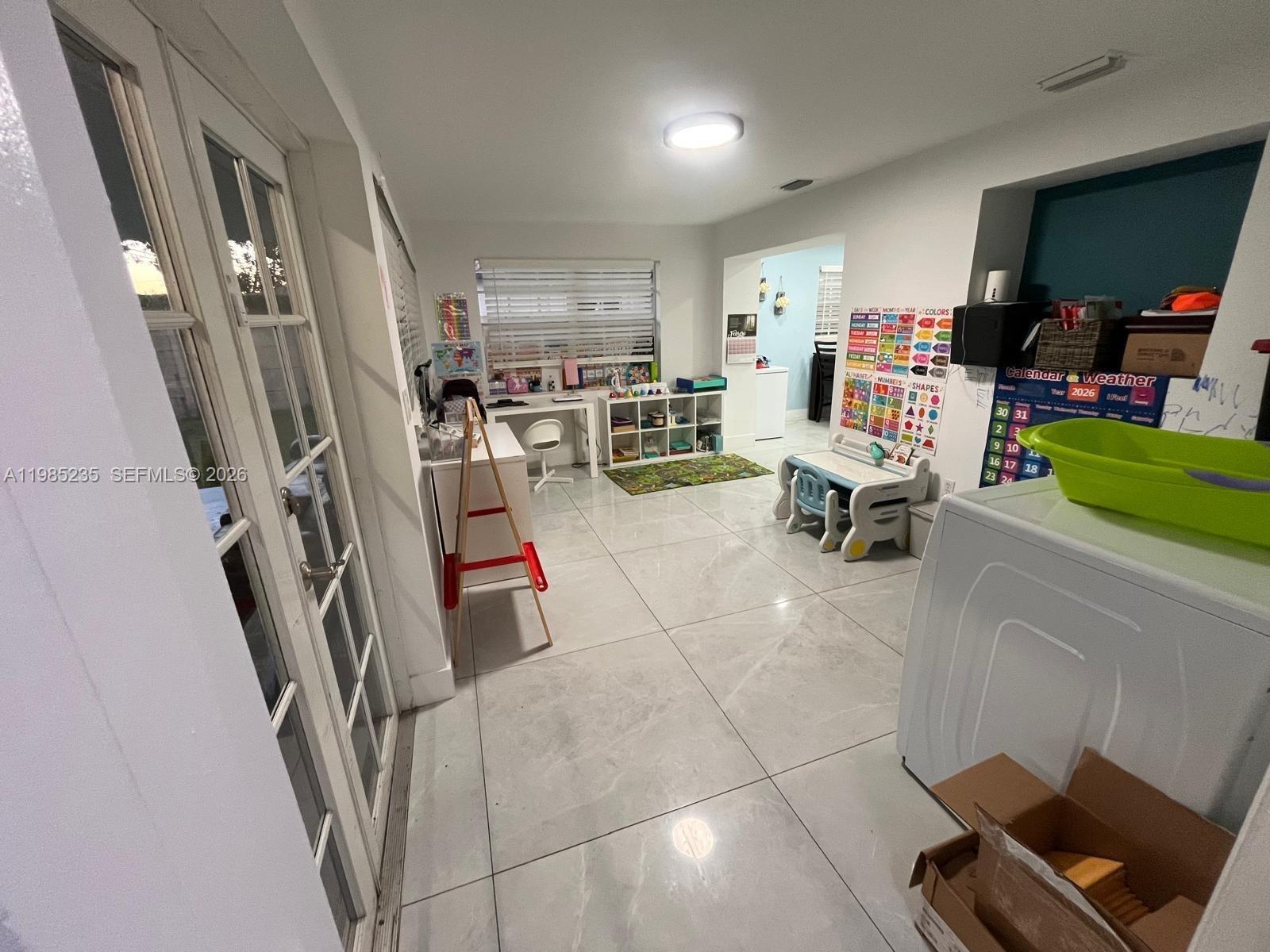 A bright playroom features large light-colored floor tiles, a desk, shelving, and educational wall charts — 9770 SW 13th Ter, Miami FL 33174, MIAMI, FL