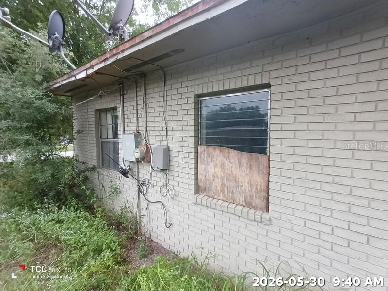 An exterior view of a brick house with a boarded-up window and utility equipment — 1114 30TH STREET NW, WINTER HAVEN, FL