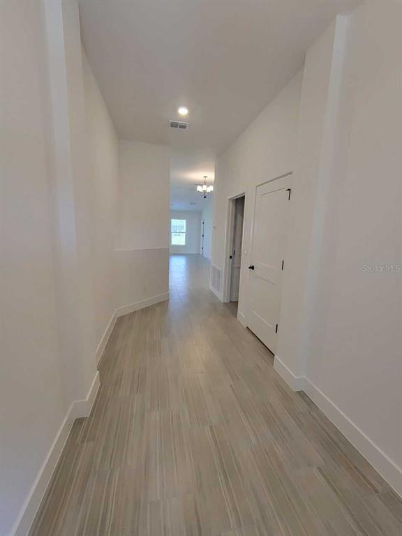 A hallway with light-colored wood-look tile flooring leads toward a bright, open living area — 4386 SW 92ND PLACE ROAD, OCALA, FL