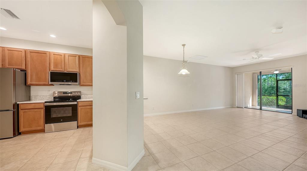A kitchen with wood cabinets and stainless appliances opens to a tiled living area — 1821 BATELLO DRIVE, VENICE, FL