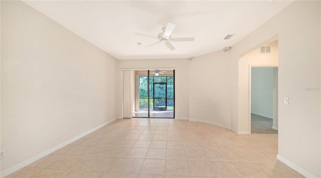 An empty room with beige tile flooring, a hanging light fixture, and a sliding glass door — 1821 BATELLO DRIVE, VENICE, FL