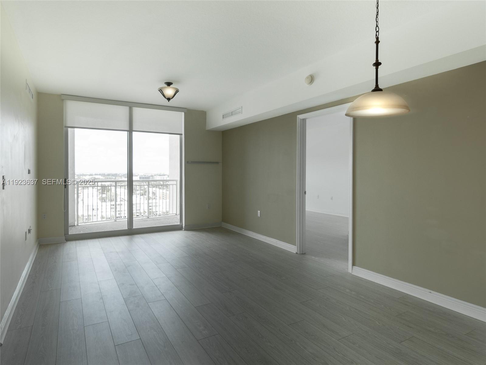 An empty room features gray wood-look flooring, a balcony with a view, and a pendant light — 1745 E Hallandale Beach Blvd # 1508W, Hallandale Beach FL 33009, HALLANDALE BEACH, FL
