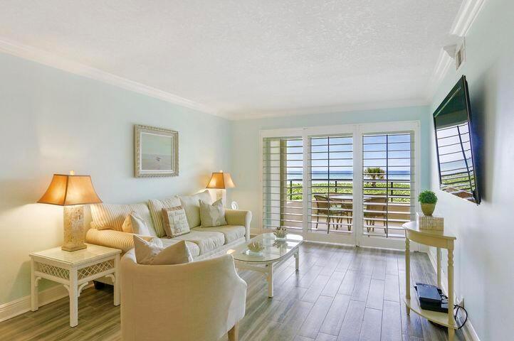 A living room with light blue walls, a beige sofa, and sliding doors overlooking the ocean — 420 Celestial Way Way # 206, Juno Beach FL 33408, JUNO BEACH, FL