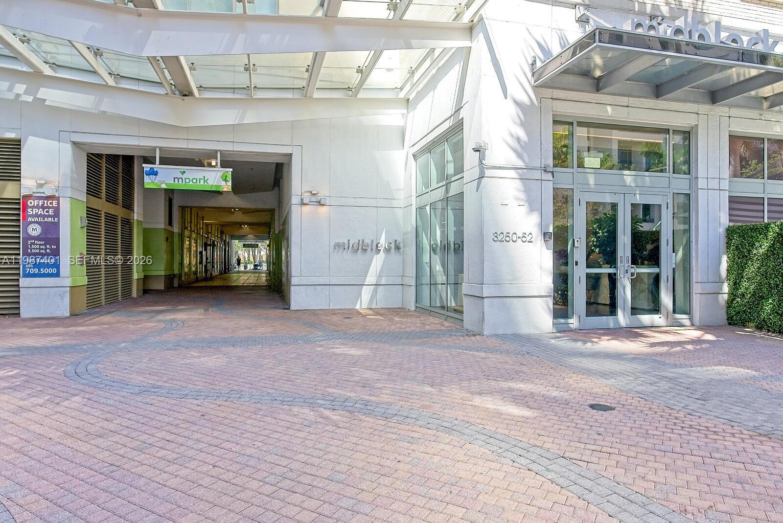 An exterior view of a modern building entrance with a brick-paved walkway and glass doors — 3250 NE 1st Ave # 1006, Miami FL 33137, MIAMI, FL