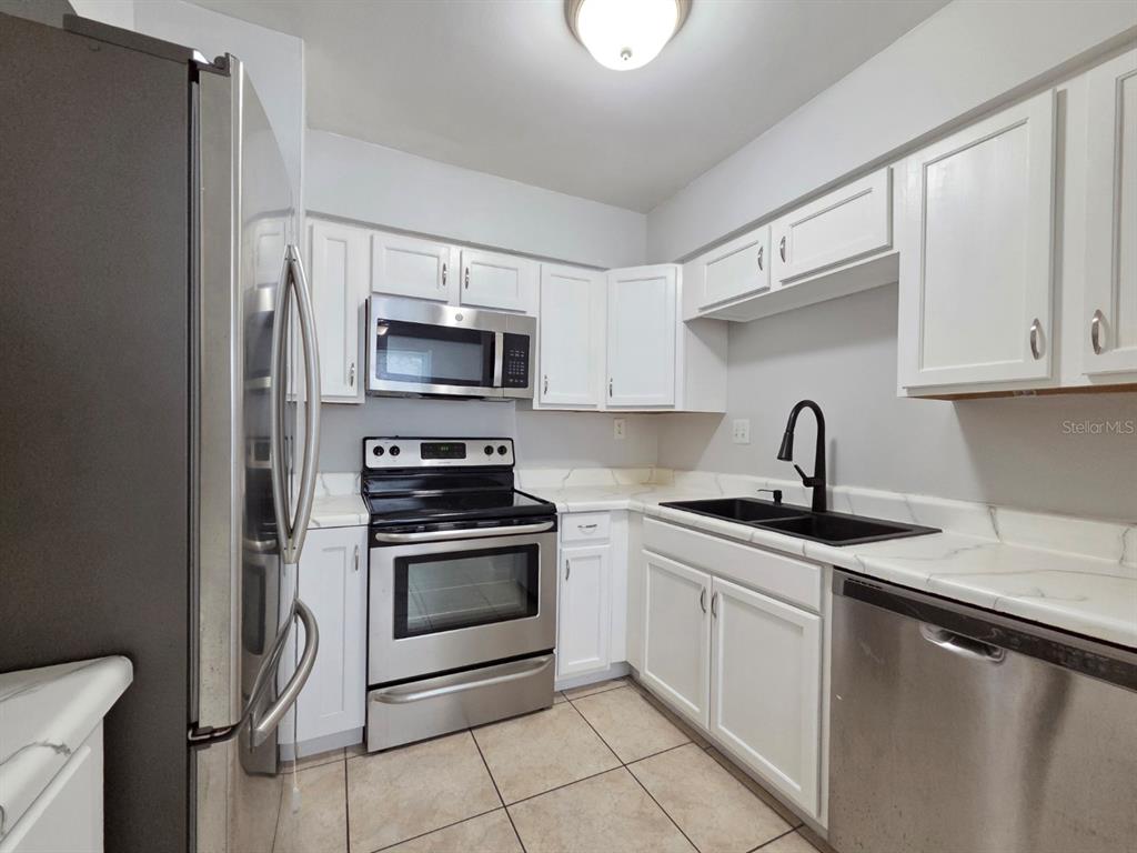 A kitchen with white cabinets, stainless steel appliances, black fixtures, and light-colored tile flooring — 3004 GEORGE MASON AVENUE UNIT K5, WINTER PARK, FL
