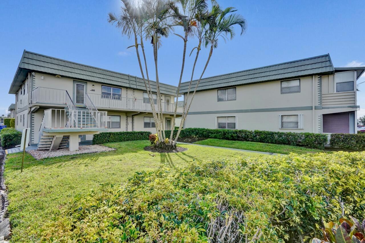A two-story apartment building features beige stucco walls, a green roof, and exterior staircases — 505 Monaco K, Delray Beach FL 33446, DELRAY BEACH, FL
