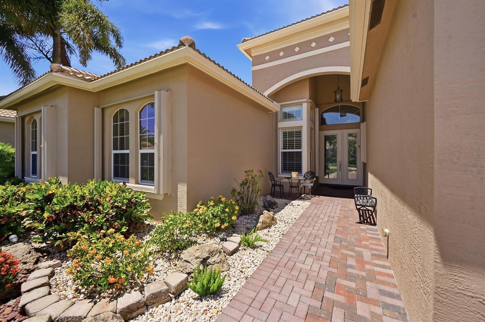 A brick walkway leads to the front entrance of a beige stucco house with landscaping — 10469 Whitewind Circle, Boynton Beach FL 33473, BOYNTON BEACH, FL
