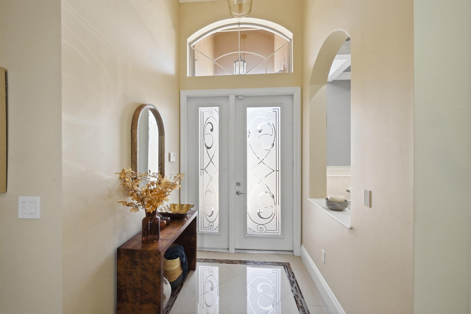 A bright entryway features a double glass-paneled front door, arched transom window, and console table — 10469 Whitewind Circle, Boynton Beach FL 33473, BOYNTON BEACH, FL