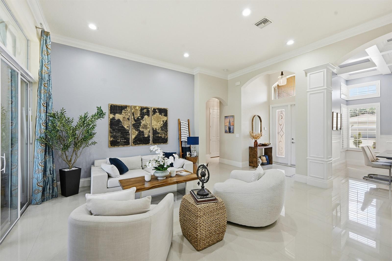 A bright living room features a white sofa, two armchairs, and a world map wall art — 10469 Whitewind Circle, Boynton Beach FL 33473, BOYNTON BEACH, FL