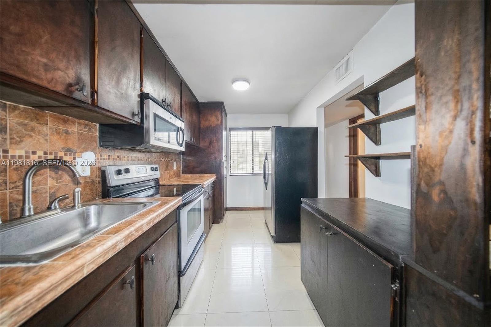 A galley-style kitchen features dark wood cabinets, tiled countertops, and black appliances — 10710 NW 7th St # 11B, Miami FL 33172, MIAMI, FL