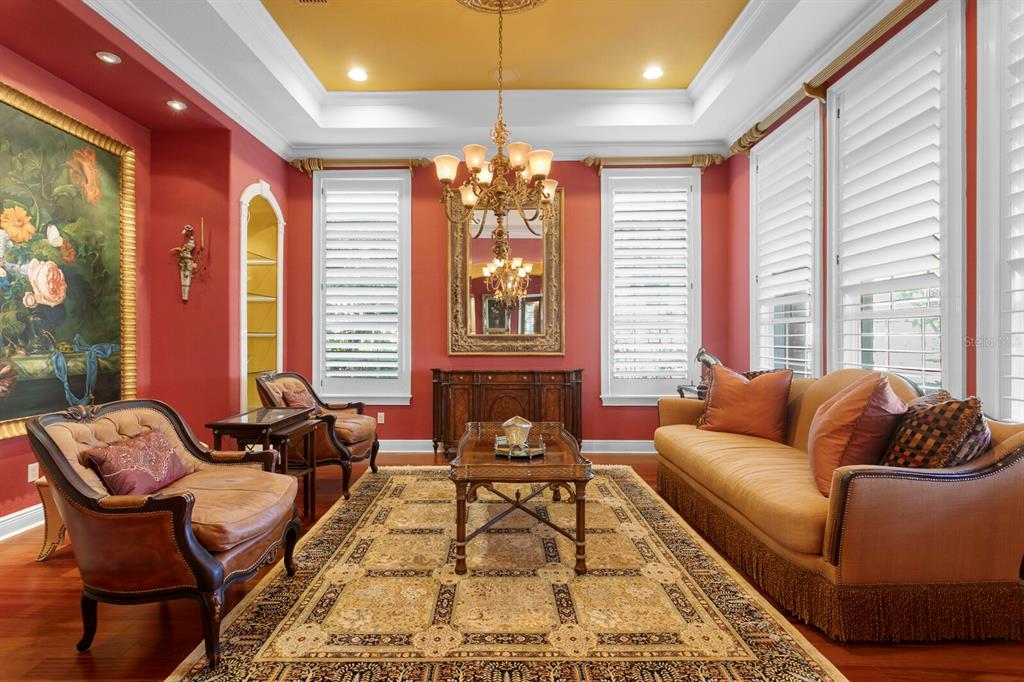A formal living room features red walls, a gold tray ceiling, and a large chandelier — 4912 YACHT CLUB DRIVE, TAMPA, FL