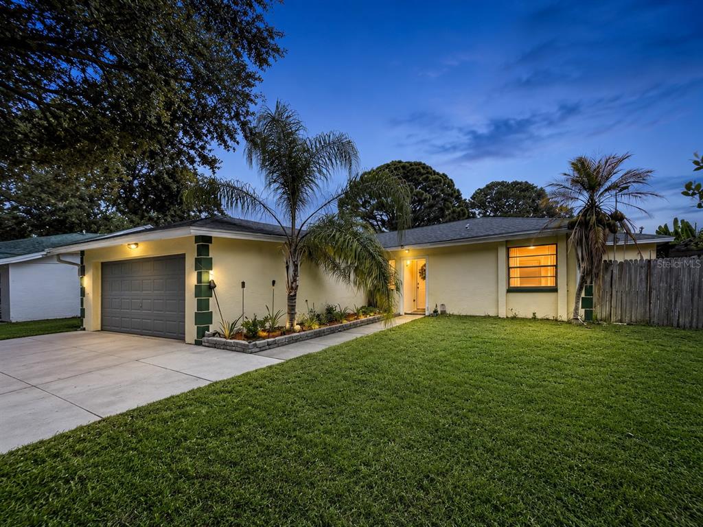 A single-story yellow house with a gray garage door and a front lawn at dusk — 6250 CEDARBROOK DRIVE N, PINELLAS PARK, FL
