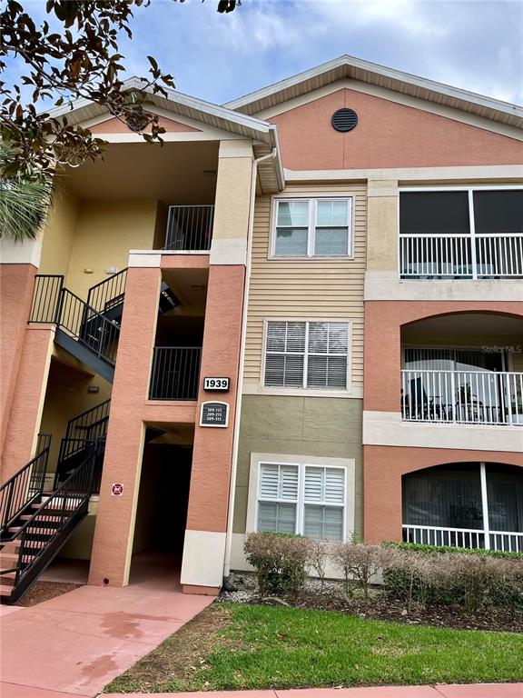 A three-story apartment building exterior features tan and peach stucco walls with metal staircases — 1939 SUMMER CLUB APT DRIVE UNIT 315, OVIEDO, FL