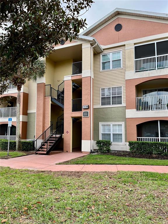 A three-story apartment building with tan stucco walls, a staircase, and screened balconies — 1939 SUMMER CLUB APT DRIVE UNIT 315, OVIEDO, FL