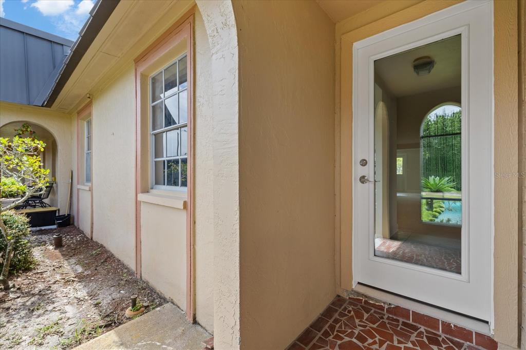 A white glass-paneled door opens onto a tiled patio beside a beige exterior wall — 4347 SUMMERSUN DRIVE, NEW PORT RICHEY, FL
