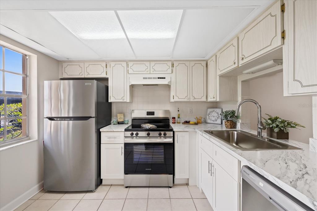 A kitchen features white cabinets, stainless steel appliances, and marble-look countertops with tile flooring — 4347 SUMMERSUN DRIVE, NEW PORT RICHEY, FL
