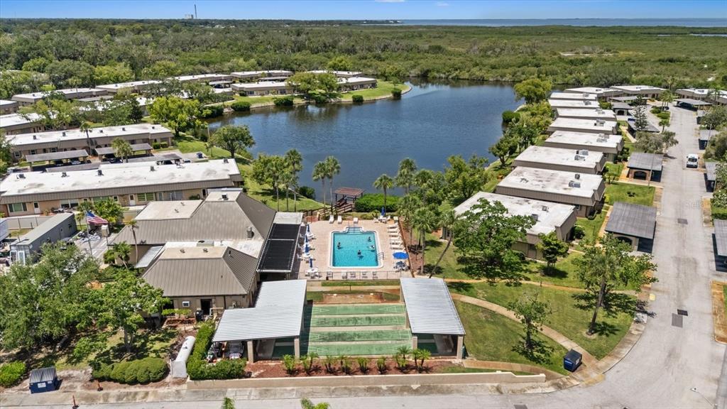 An aerial view shows a residential complex with a swimming pool, shuffleboard courts, and lake — 4347 SUMMERSUN DRIVE, NEW PORT RICHEY, FL