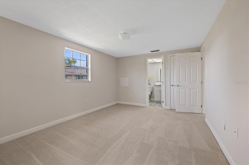 A bedroom with beige carpet, light-colored walls, a window, and an attached bathroom doorway — 4347 SUMMERSUN DRIVE, NEW PORT RICHEY, FL