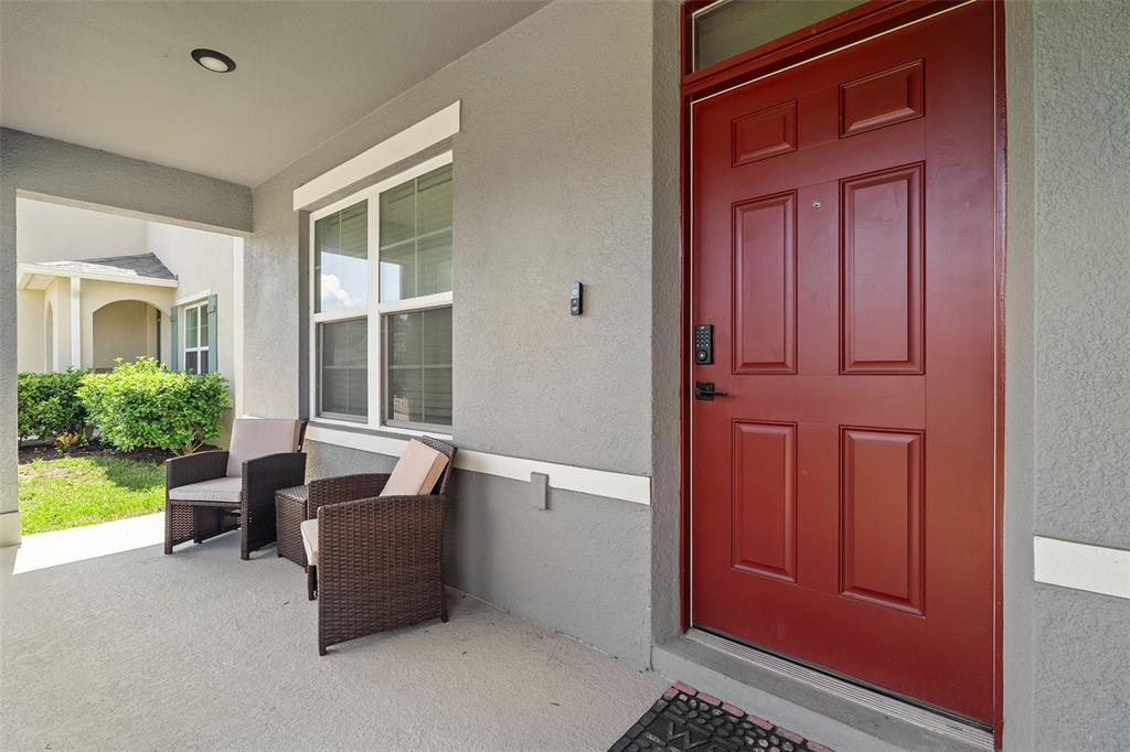 A covered front porch features a red door, two wicker chairs, and a window — 2533 HARMONIA HAMMOCK ROAD, HARMONY, FL
