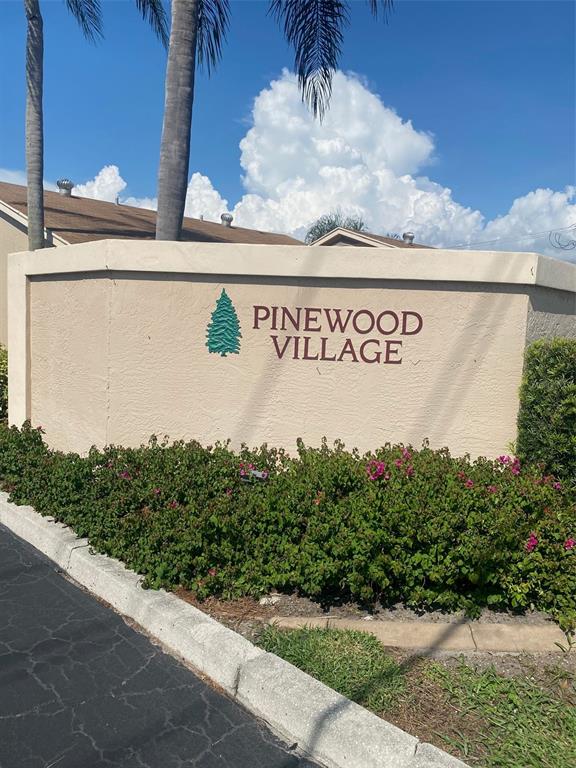 A beige stucco sign for Pinewood Village stands in front of a building and landscaping — 2763 WOODGATE LANE UNIT 208, SARASOTA, FL