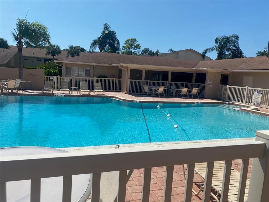 A swimming pool with a safety rope and surrounding patio furniture sits before a building — 2763 WOODGATE LANE UNIT 208, SARASOTA, FL