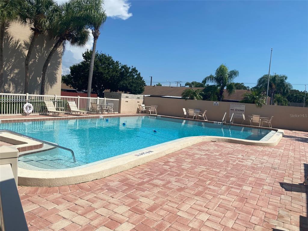 An outdoor swimming pool with a brick paver deck and lounge chairs under a clear sky — 2763 WOODGATE LANE UNIT 208, SARASOTA, FL
