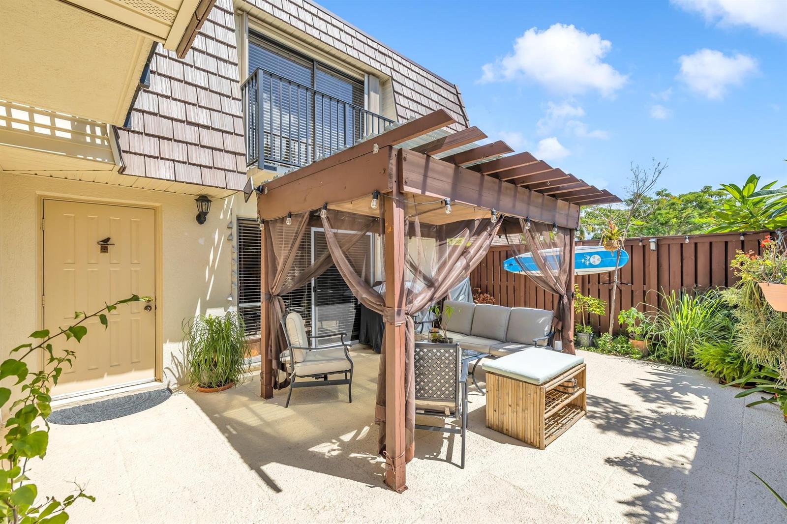 A patio features a wooden pergola with curtains over outdoor furniture and a beige house — 2776 SW 15th Street, Deerfield Beach FL 33442, DEERFIELD BEACH, FL
