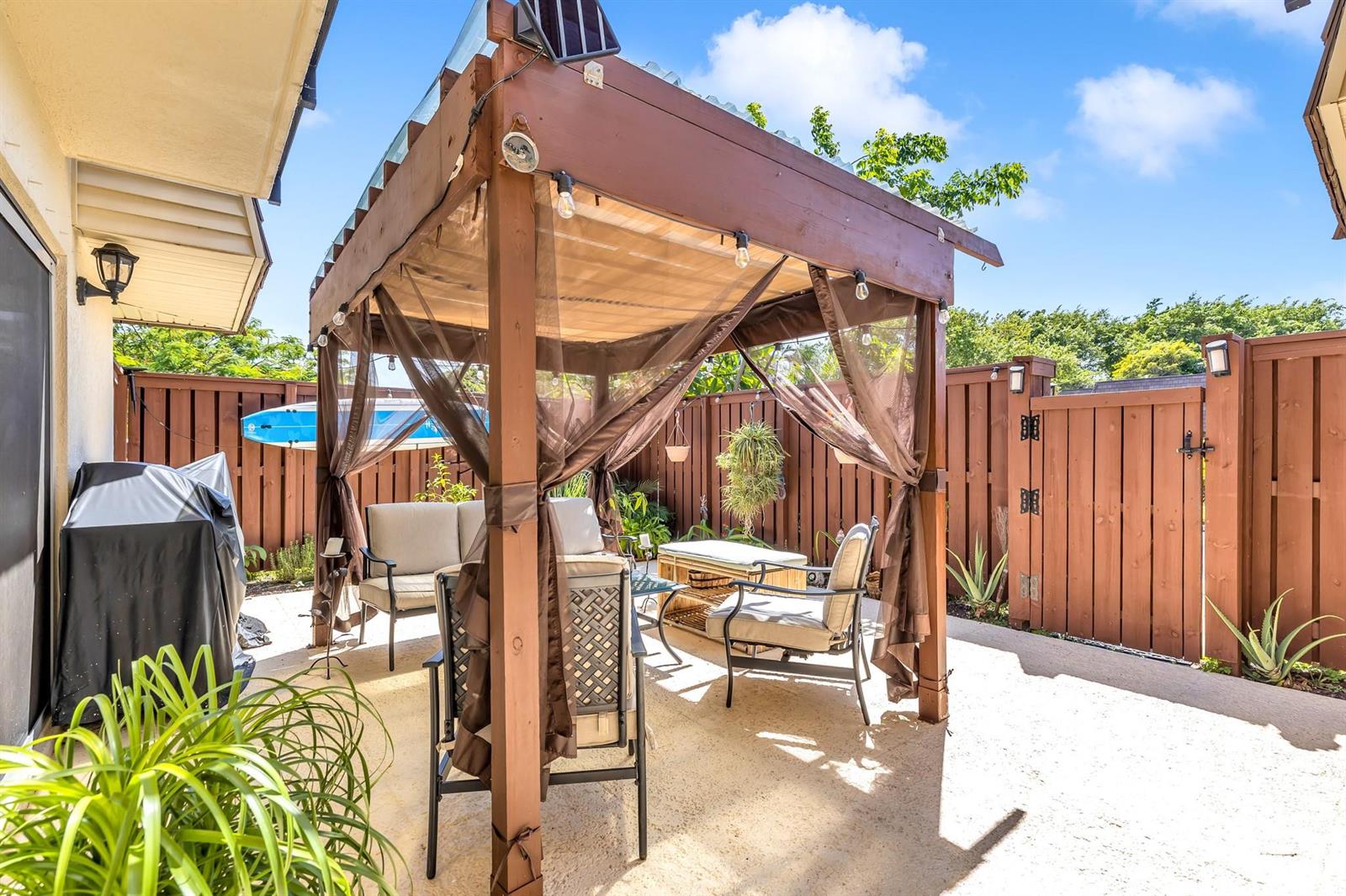 A wooden pergola with curtains and patio furniture sits on a concrete backyard patio — 2776 SW 15th Street, Deerfield Beach FL 33442, DEERFIELD BEACH, FL