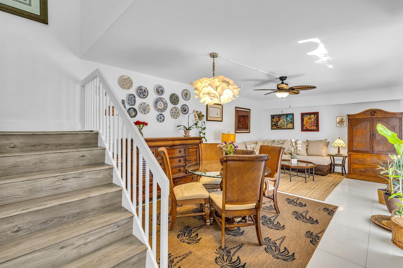 A dining area with a glass table and wicker chairs sits beside a wooden staircase — 2776 SW 15th Street, Deerfield Beach FL 33442, DEERFIELD BEACH, FL