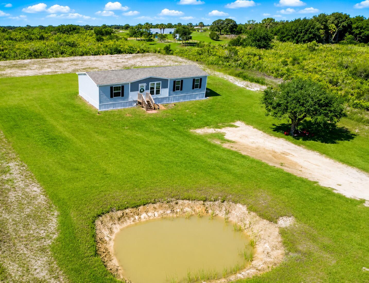 An aerial view shows a manufactured home on a grassy lot with a small pond — 18720 NW 242nd Street, Okeechobee FL 34972, OKEECHOBEE, FL